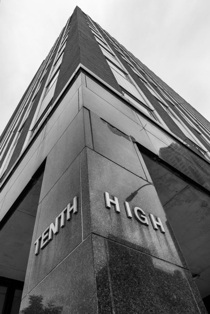 Black and white image looking up at the Century Link building at Tenth and High in Des Moines, Iowa. The lettering at the corner reads TENTH on one side of the front column and HIGH on the other.