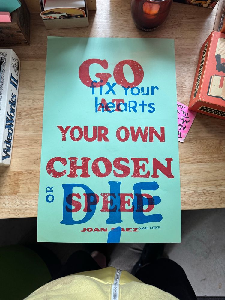 Silk screen poster on green paper that’s says, 1) Go at your own chosen speed - Joan Baez (in red), and 2) Fix your hearts or die - David Lynch (in blue)