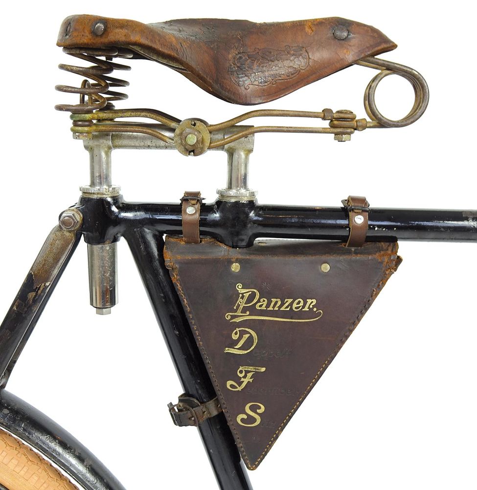 Ausschnit eines Fahrrads mit altem Ledersattel und zweifacher Befestigung des Sattels. Darunter eine Rahmen-Ledertasche mit dem Aufdruck "Panzer DFS"