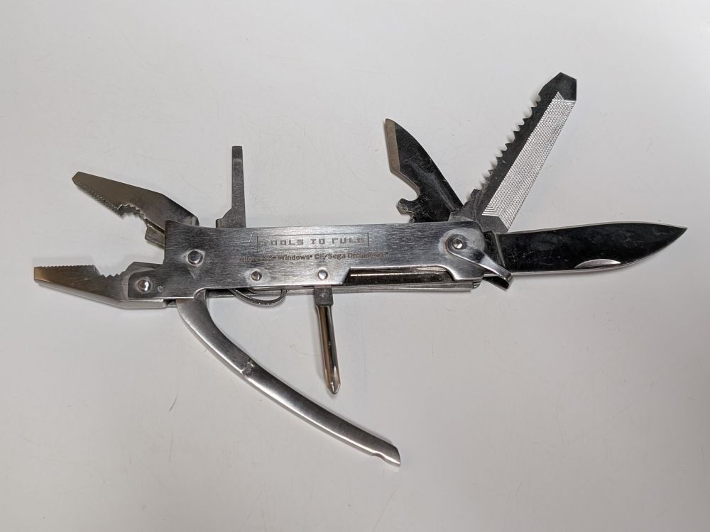 A silver-coloured pocket multi-tool with several tools extended on a white background. Visible are: pliers, wire cutters, flat and Phillips-head screwdrivers, can opener, saw, file, knife, and pick.