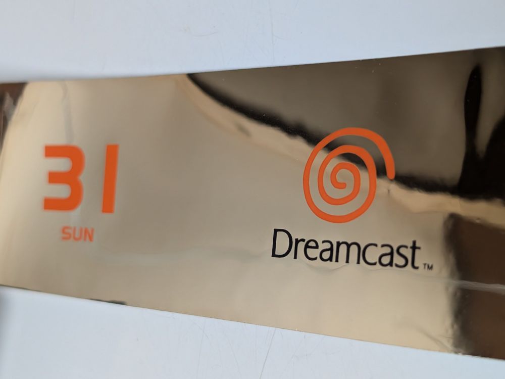 A strip of reflective silver material, upon which is printed the following:
An orange number "31" atop the letters "SUN";
The Japanese Dreamcast logo with an orange swirl atop the stylized word "Dreamcast™" in black.