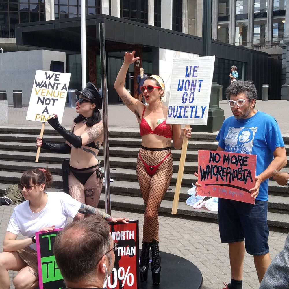 Fired Up Stilettos representatives on the steps of the New Zealand Parliament, calling for the nation's politicians to recognize its petition to improve strippers working conditions in Aotearoa. @sjvita joins them, holding a sign that says No More Whorephobia, alongside signs that say 'We Won't Go Quietly' and 'We Want A Venue Not A Pimp.