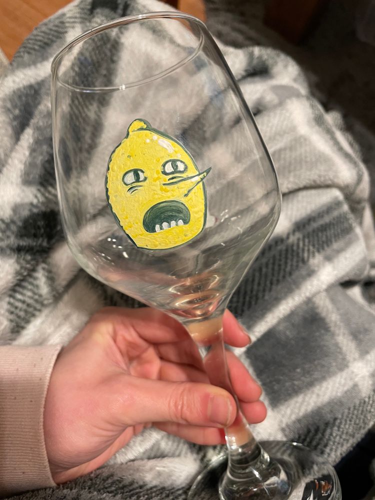 A stemmed wine glass with a hand painted Lemongrab from AT. He looks forward and screams into oblivion.