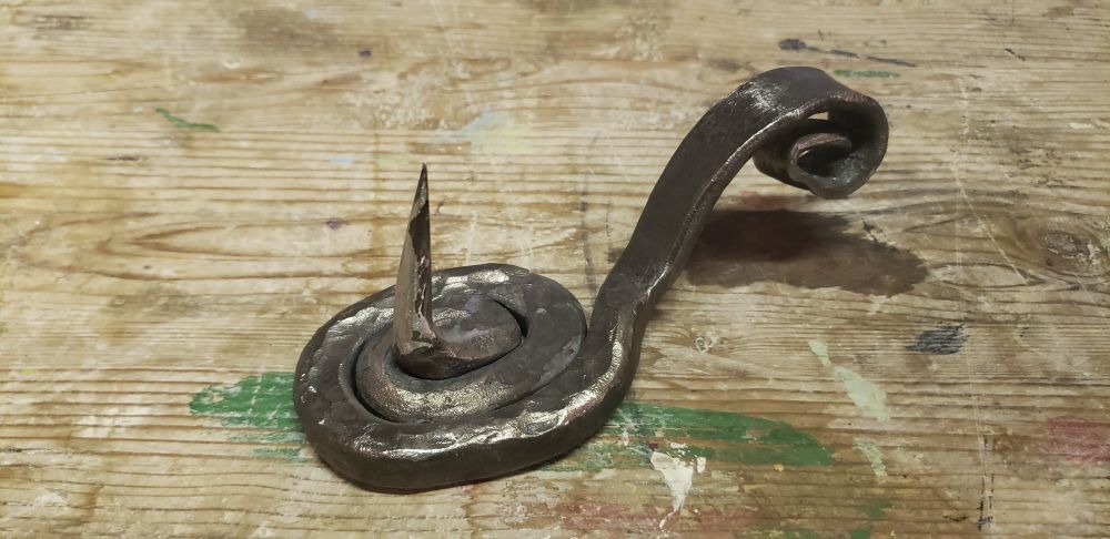 A metal spike that coils around itself at its base, then flattens and curves upward slightly into a handle, ending in a scroll.