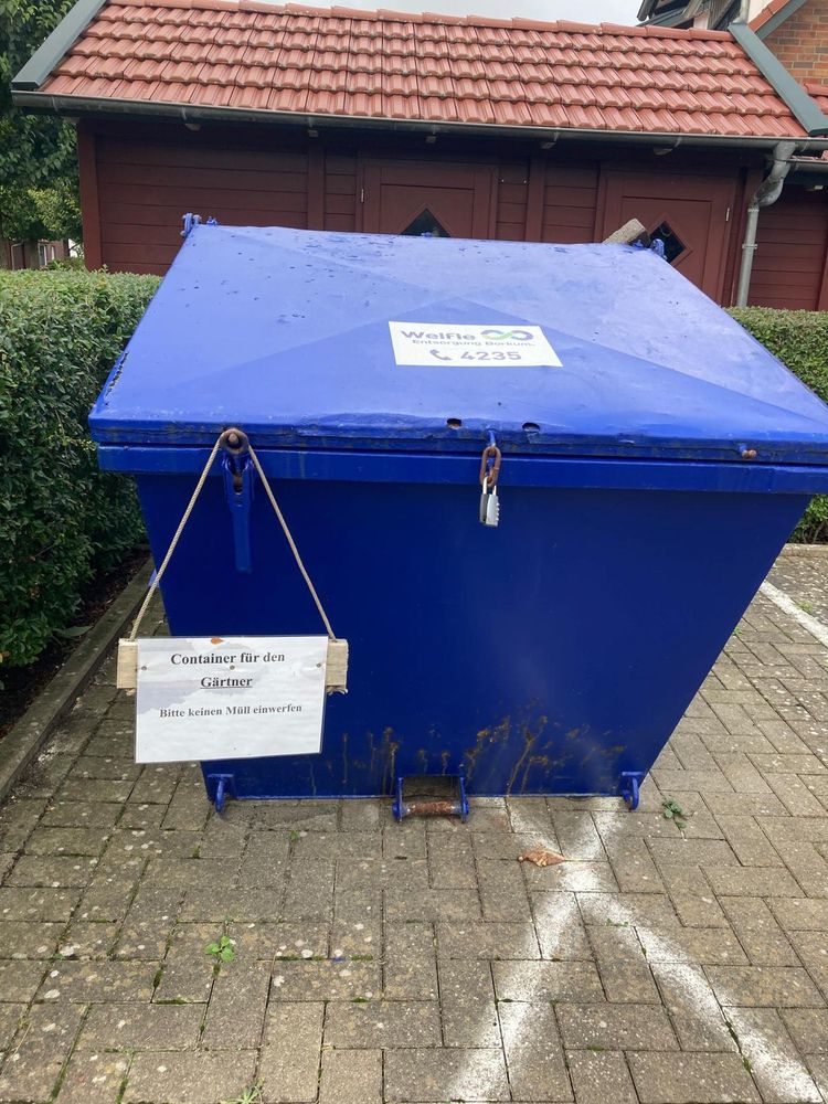 Blauer Schüttcontainer mit Deckel auf einem Parkplatz, vor einer Hecke. Daran ein Schild mit einem Strick befestigt "Container für den Gärtner, bitte keinen Müll einwerfen"

Aufkleber auf dem Container"Welfle Borkum" mit Telefonnummer 