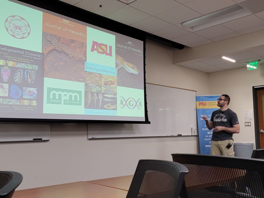 Dr. Brendan Pinto on the right, pointing to a slide showing his scientific trajectory including college in Iowa, PhD in Wisconsin, and now researching at ASU.