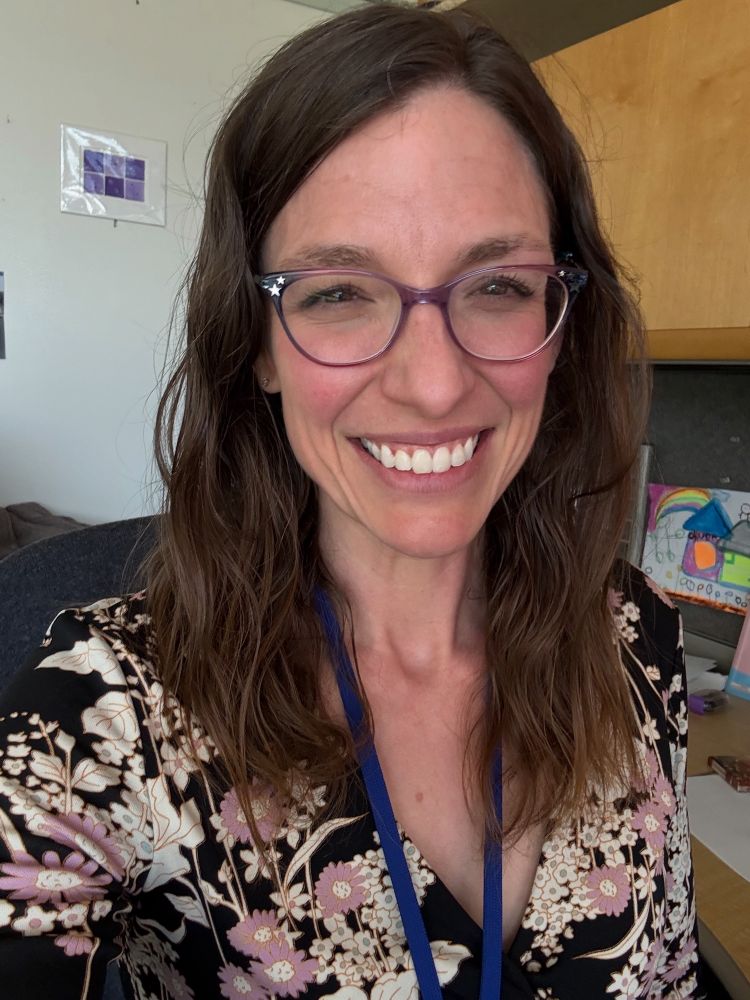 Selfie of a scientist with brown hair, purple glasses, smiling, before giving a remote presentation 