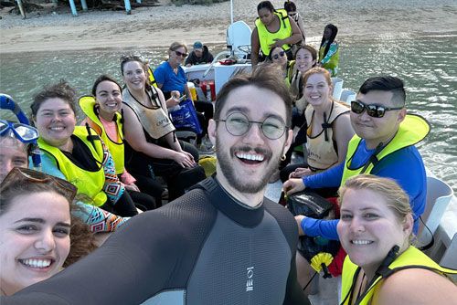 Group of people in life jackets smiling on a boat, ready for a water activity.