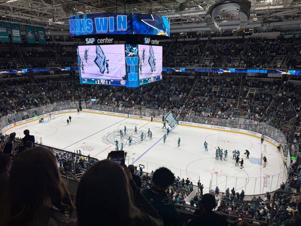 A picture of a SJ Sharks hockey game where the Jumbotron is flashing “SHARKS WIN” 