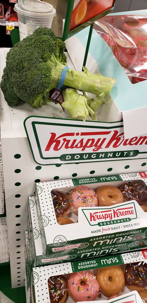 Picture of Krispy Kreme donut display, with a single bundle of broccoli abandoned on top of it