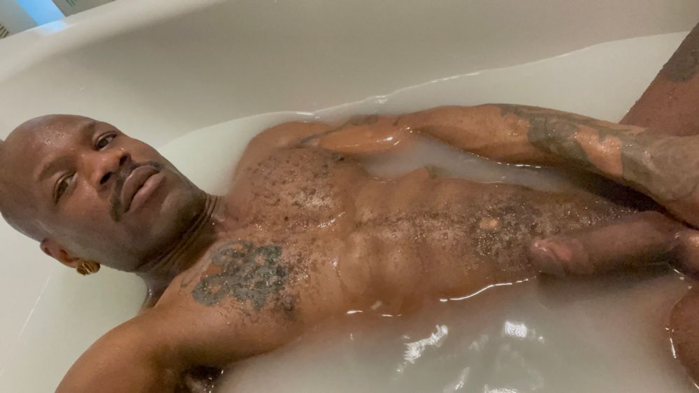 Bishop is flexing in salt bath at home. They look to the camera, seductively