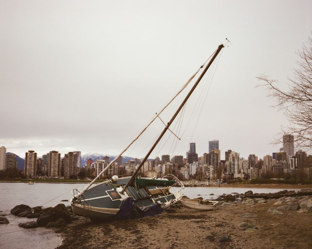 A medium format film photo taken of a sail boat that is stuck on the beach in Vancouver, Canada. The city skyline and mountains are visible in the background 
