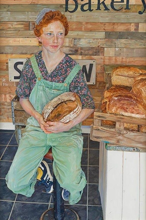 Red-haired teenaged woman, in dungarees and tightly patterned shirt, wearing cap and blue sneakers, sits on stool, holding basket of fresh-baked bread, as she look off to the right  