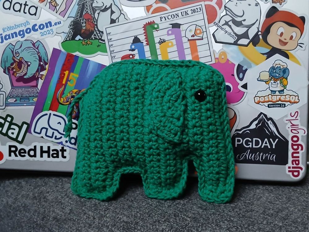 Adorable dark green crochet elephant, leaning against a laptop lid covered in stickers