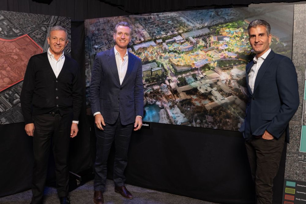 Bob Iger, Gavin Newsom, and Josh D’Amaro pose with Disneyland Forward concept art.