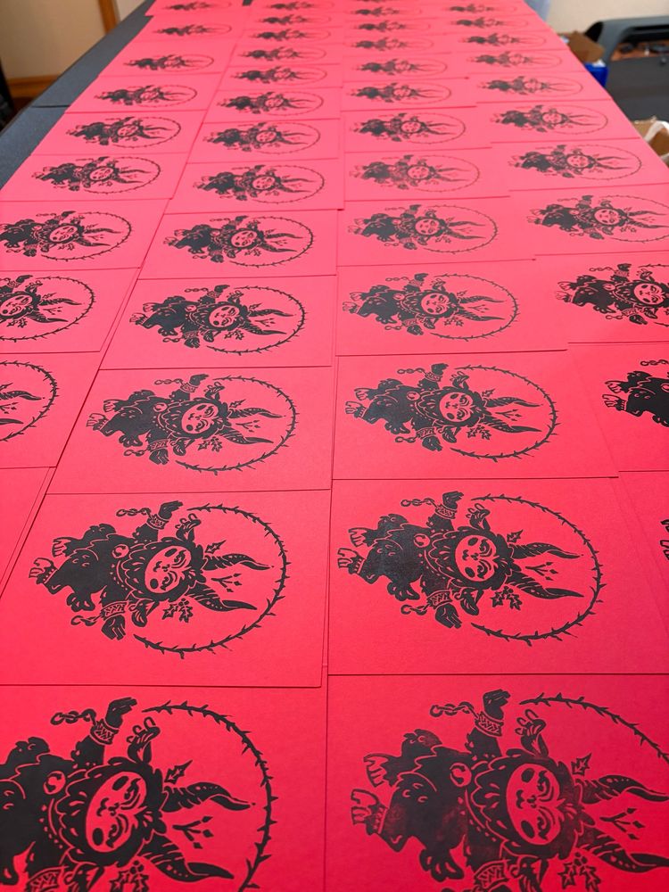 A table top covered in red greeting cards with black block prints of a cute hopping Krampus on the fronts.