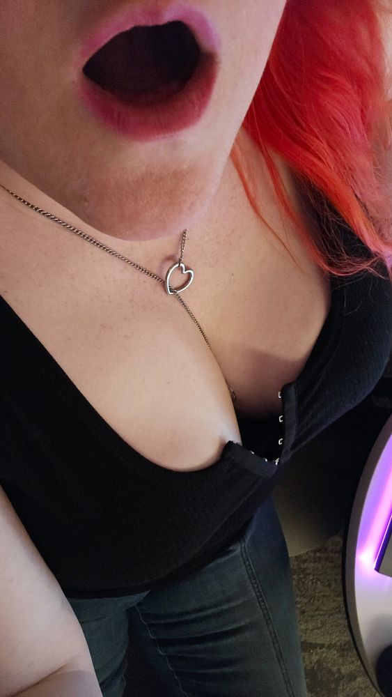 Selfie. Red haired woman looking at the camera with her tits hanging out of her black top. She's opening her mouth.