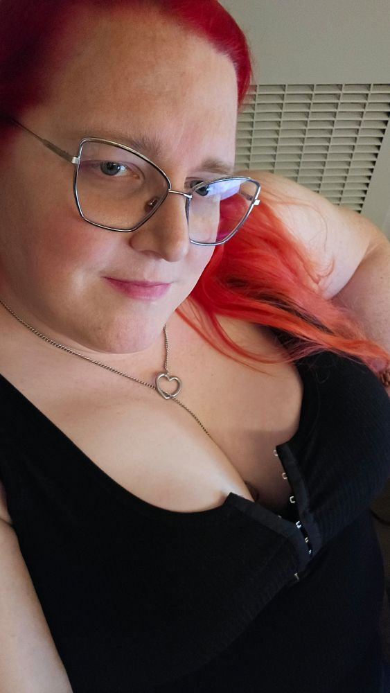 Selfie. Red haired woman looking at the camera with her tits hanging out of her black top
