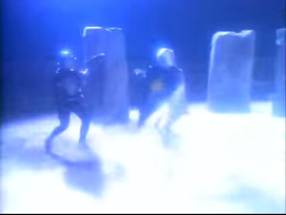 A bright flash of white light as two armoured figures with shields battle with parts of a not real Stonehenge visible behind them. From the Twilight Zone segment “The Last Defender of Camelot.”