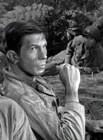 Leonard Nimoy in the Twilight Zone episode “The Quality of Mercy”, seared, making a fist, a man in WW2 army uniform behind him alongside jungle bits.