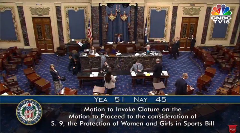 A screenshot of the U.S. Senate chamber during a session. Several senators and staff members are present, some standing and talking while others are seated at their desks. The chamber has blue carpeting with gold accents, wooden desks, and a raised platform where the presiding officer is seated. Above the chamber doors, an inscription reads "E PLURIBUS UNUM."

At the bottom of the image, a text overlay shows the results of a vote:
"YEA 51 NAY 45"
It states:
"Motion to Invoke Cloture on the Motion to Proceed to the consideration of S. 9, the Protection of Women and Girls in Sports Bill."

In the top right corner, the CNBC TV18 logo is visible, indicating that this was a televised broadcast. In the bottom right corner, a red button labeled "SUBSCRIBE NOW" is also present.