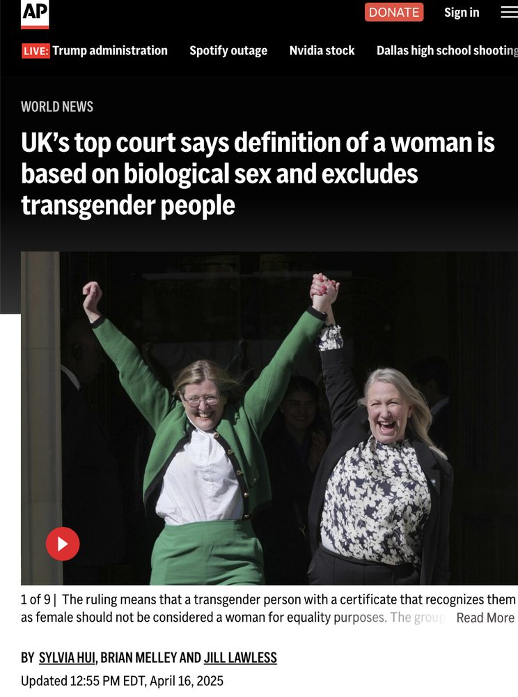 Screenshot of an Associated Press article titled “UK’s top court says definition of a woman is based on biological sex and excludes transgender people.” The subheadline reads: “The ruling means that a transgender person with a certificate that recognizes them as female should not be considered a woman for equality purposes.” Below the headline is a photo of two smiling women holding hands and raising their arms in apparent celebration. One wears a green cardigan and pants; the other wears a black blazer and floral blouse. The article is by Sylvia Hui, Brian Melley, and Jill Lawless, and was updated at 12:55 PM EDT on April 16, 2025.