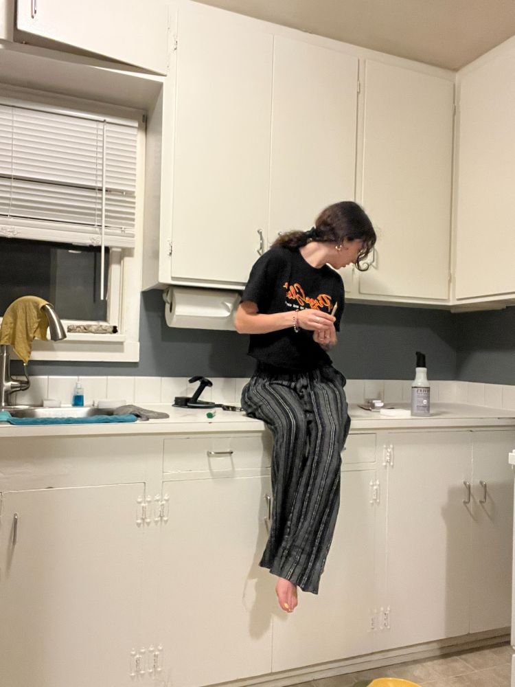 me sitting on the counter in the kitchen (white cabinets  blue walls) about to light a joint 