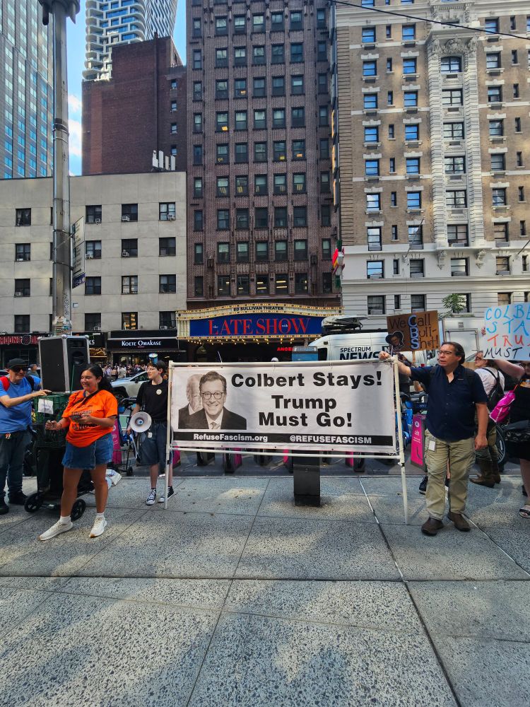 Crowd across the street from The Ed Sullivan Theater where The Late Show With Stephen Colbert films. Under the show's marquee is a sign that reads "Colbert Stays! Trump Must Go!"
