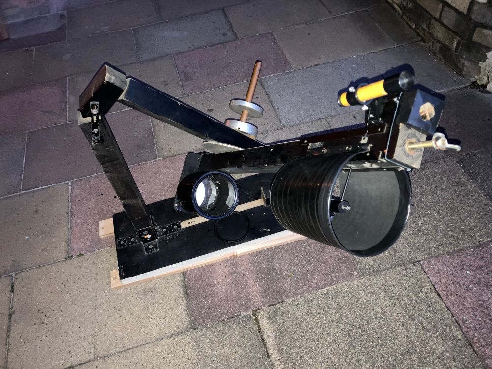 Ein selbstgebautes Teleskop. Es besteht aus mehreren Holzteilen und einem Gegengewicht. Man erkennt einen Spiegel und ein Zielfernrohr.