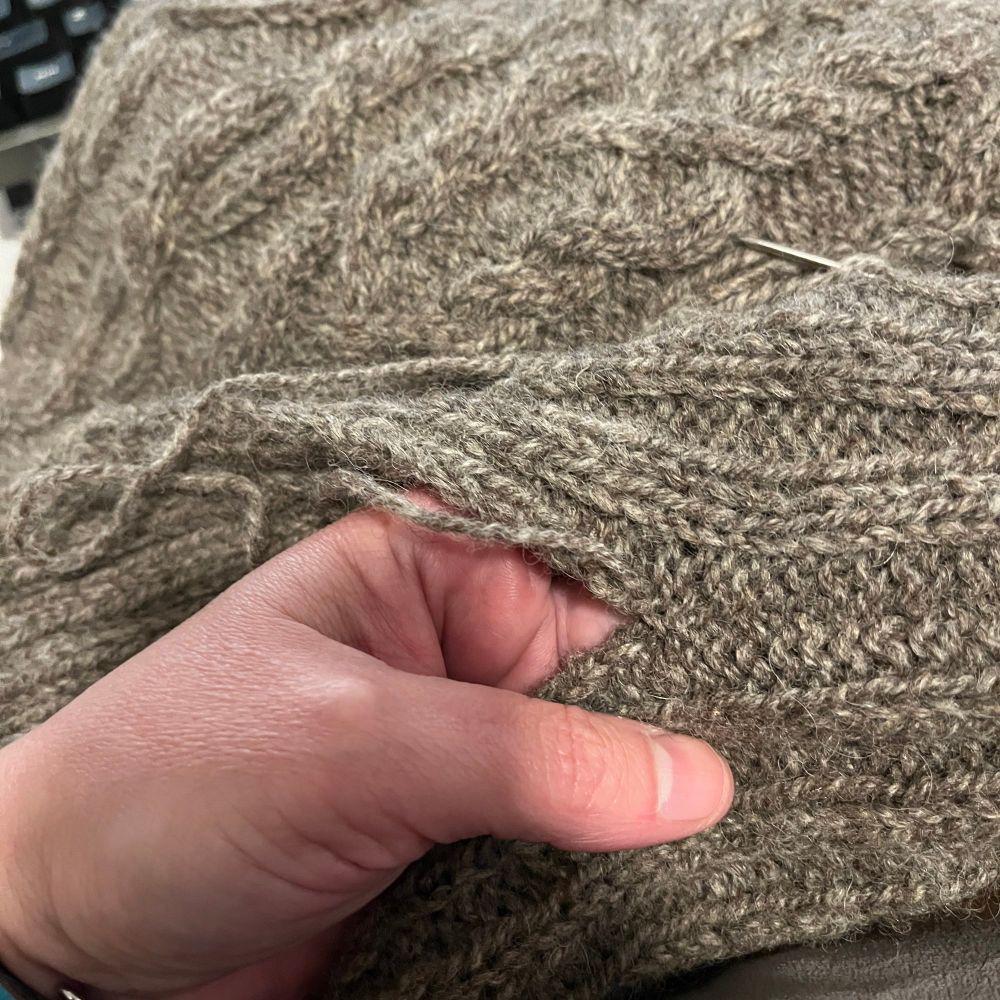 Image shows a close up of a hand holding a brown-grey piece of knit fabric 