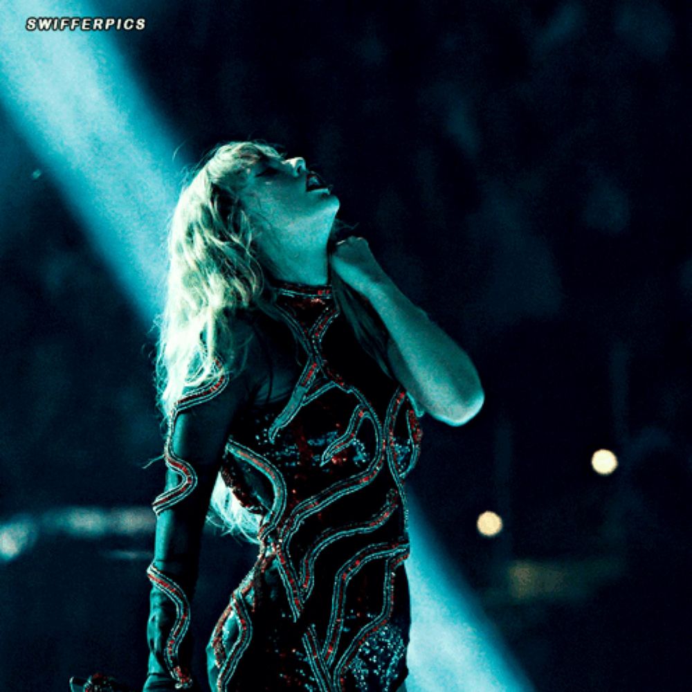 a woman in a black dress is singing into a microphone with swifterpics written below her