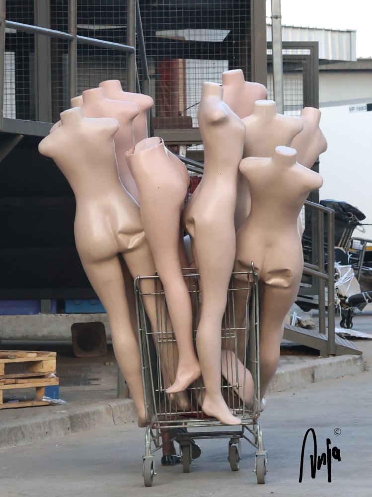 Damaged mannequins standing upright in a shopping trolley being wheeled through town. 