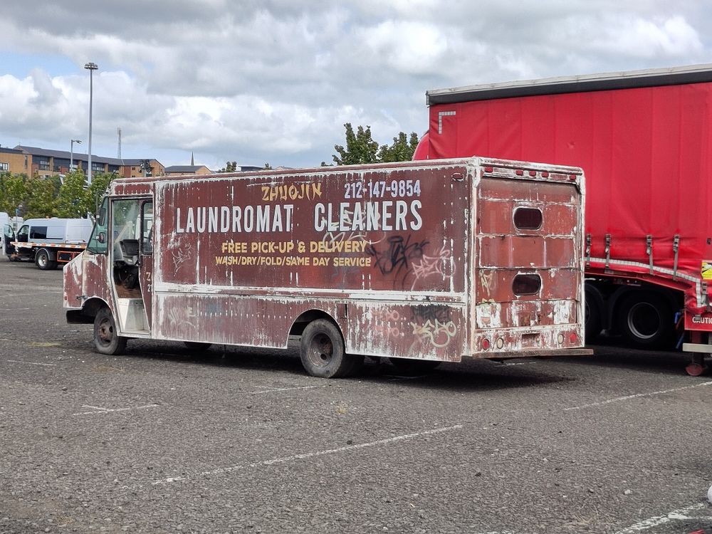 A large brown van with faded paint, some graffiti and signage for ZHHOJIN 212-147-9854 LAUNDROMAT CLEANERS