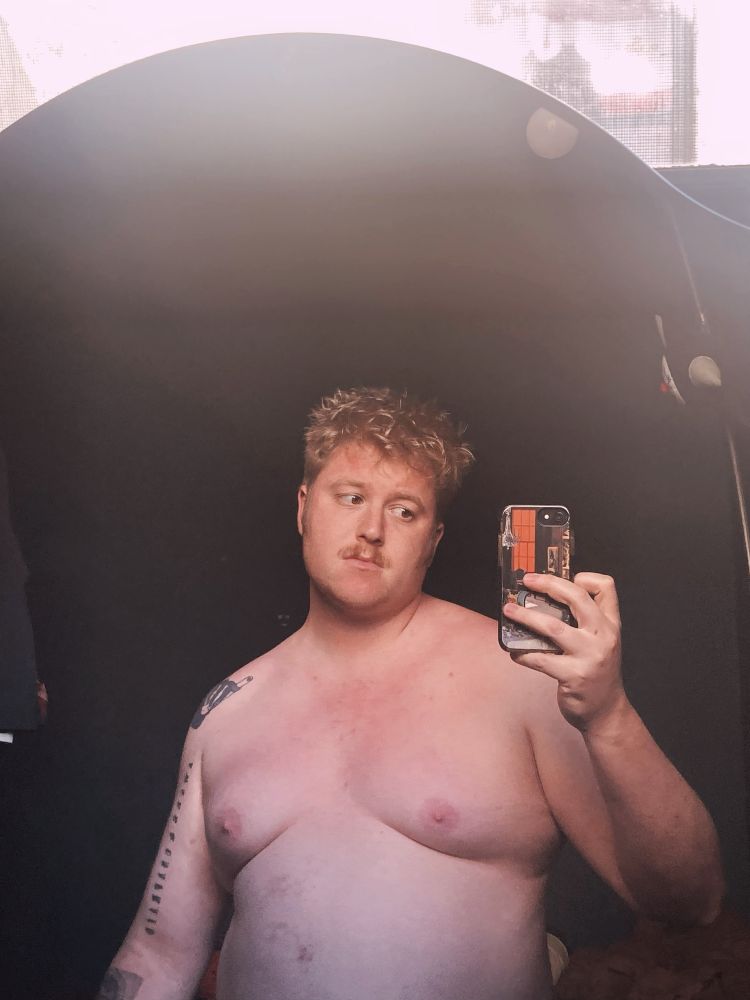 Mirror selfie, from naked stomach up, a blonde Melon looking wistfully at the phone