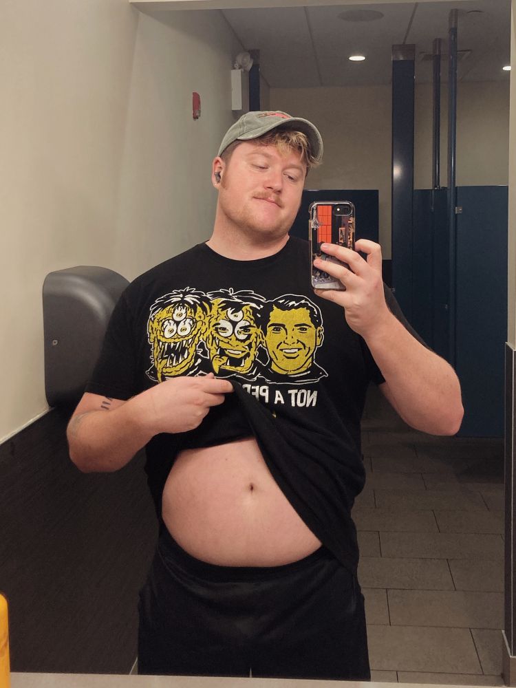 Mirror selfie of Melon, in the gym bathroom, lifting up his shirt to show his belly