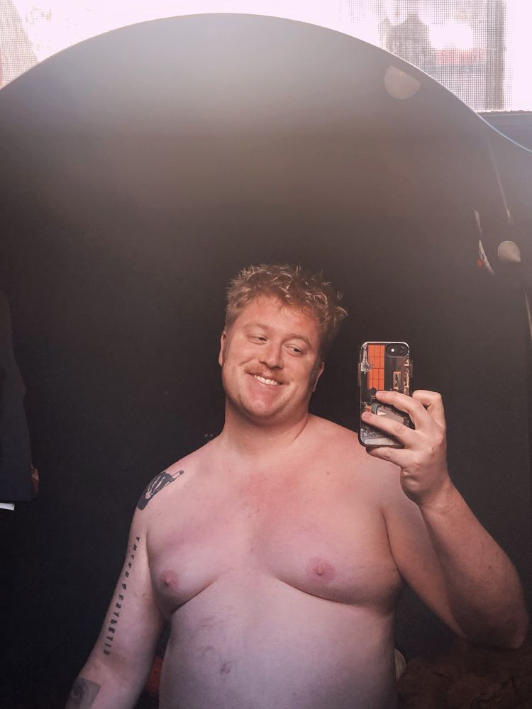 Mirror selfie, from naked stomach up, a blonde Melon looking smilingly at the phone