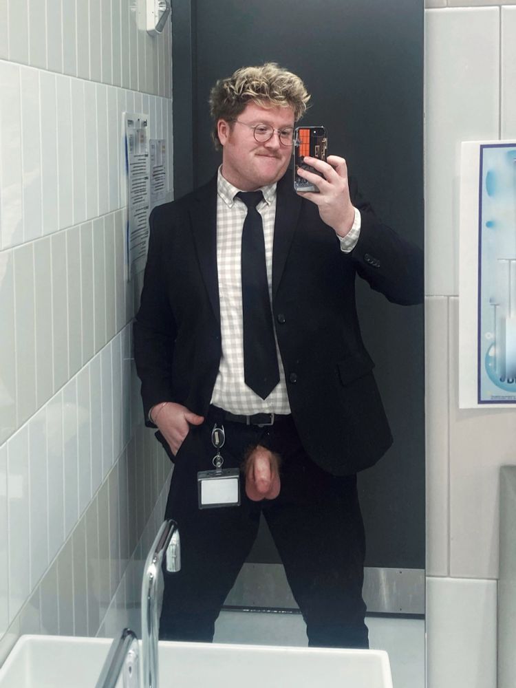 Mirror selfie of a man in a full suit. His fly is down and his dick and balls are on display. He is smirking because he is finally off work.