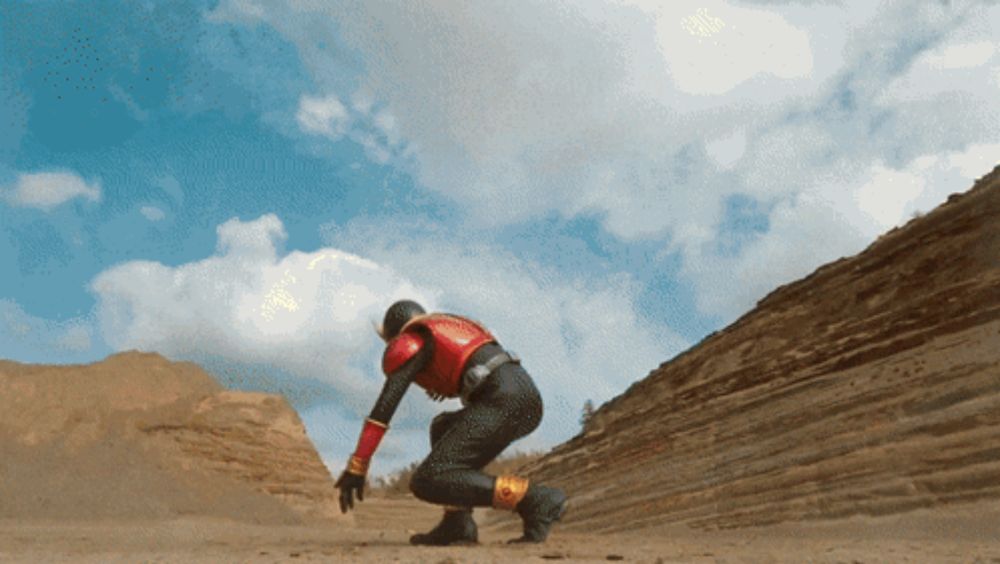 a man in a red and black superhero costume is kneeling in the sand