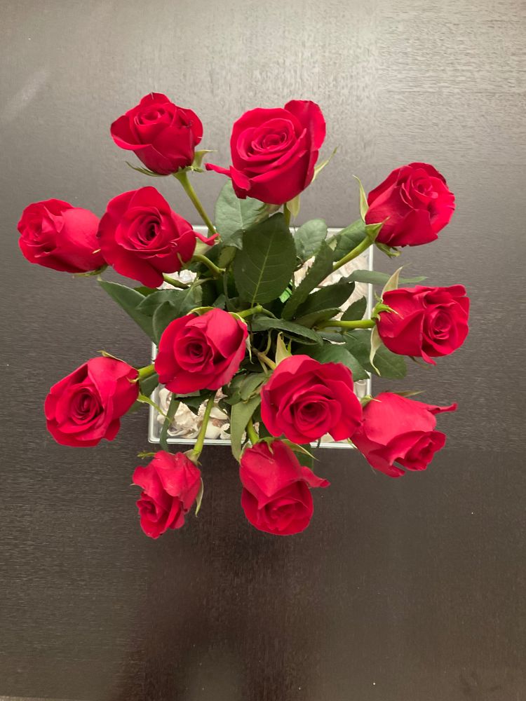 A bird’s eye view of a dozen red roses on a black coffee table.