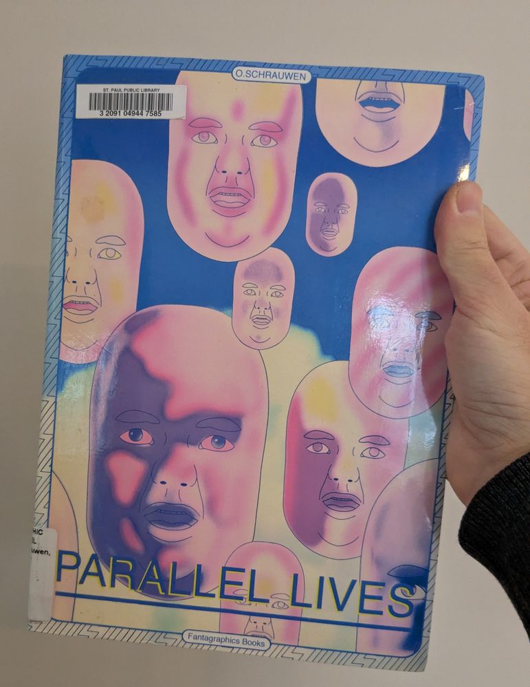 A hand holding a book titled parallel lives with pink floating heads