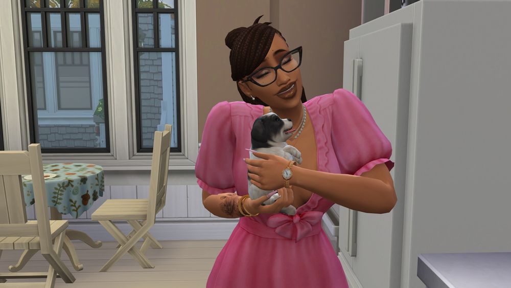 Female Young Adult "The Sims 4" sim holding a small black and white fluffy puppy in a kitchen setting. She is wearing a pink dress with puffed sleeves, has on a necklace, and is wearing a watch. She has light brown skin, wears cat-eye glasses, and has braided hair. In the background, there are large windows allowing natural light to enter, and a round table with a patterned tablecloth is visible, along with wooden chairs. The kitchen has a modern design, with a refrigerator and light-colored walls.