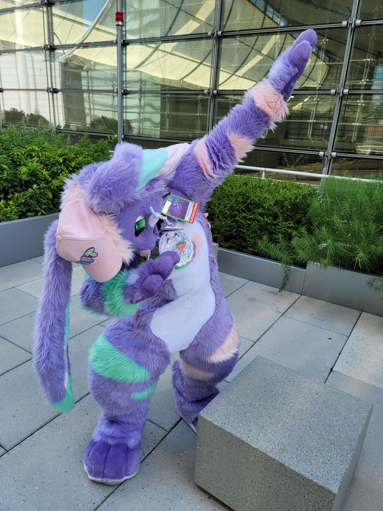 Purple bunny fursuiter doing a sick dab outside in a park.