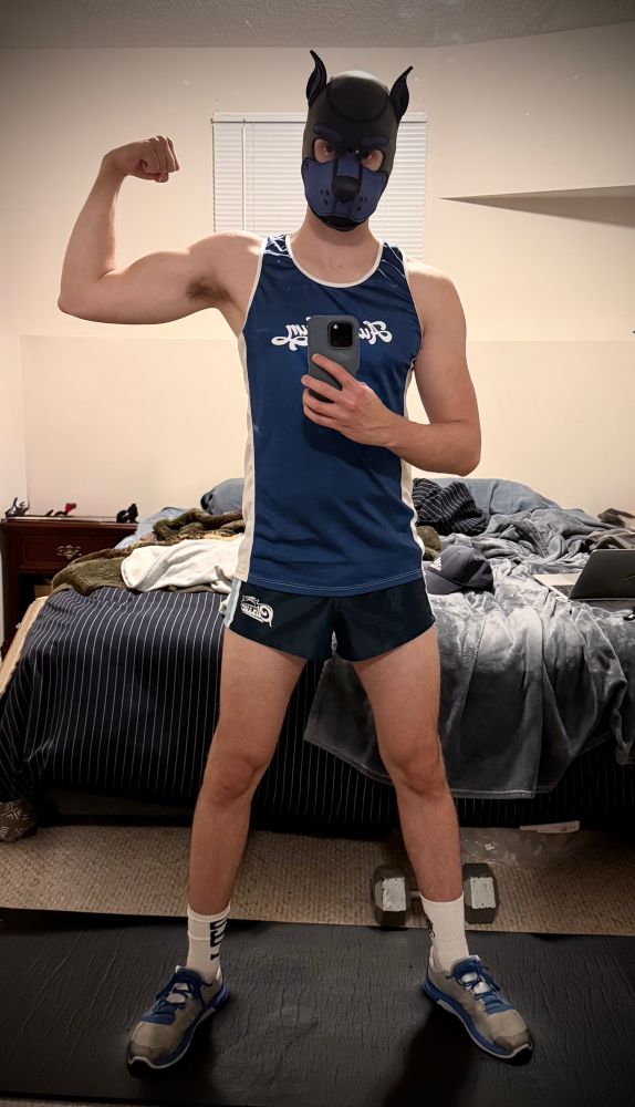 Gay man with pup hood flexing bicep in workout gear 