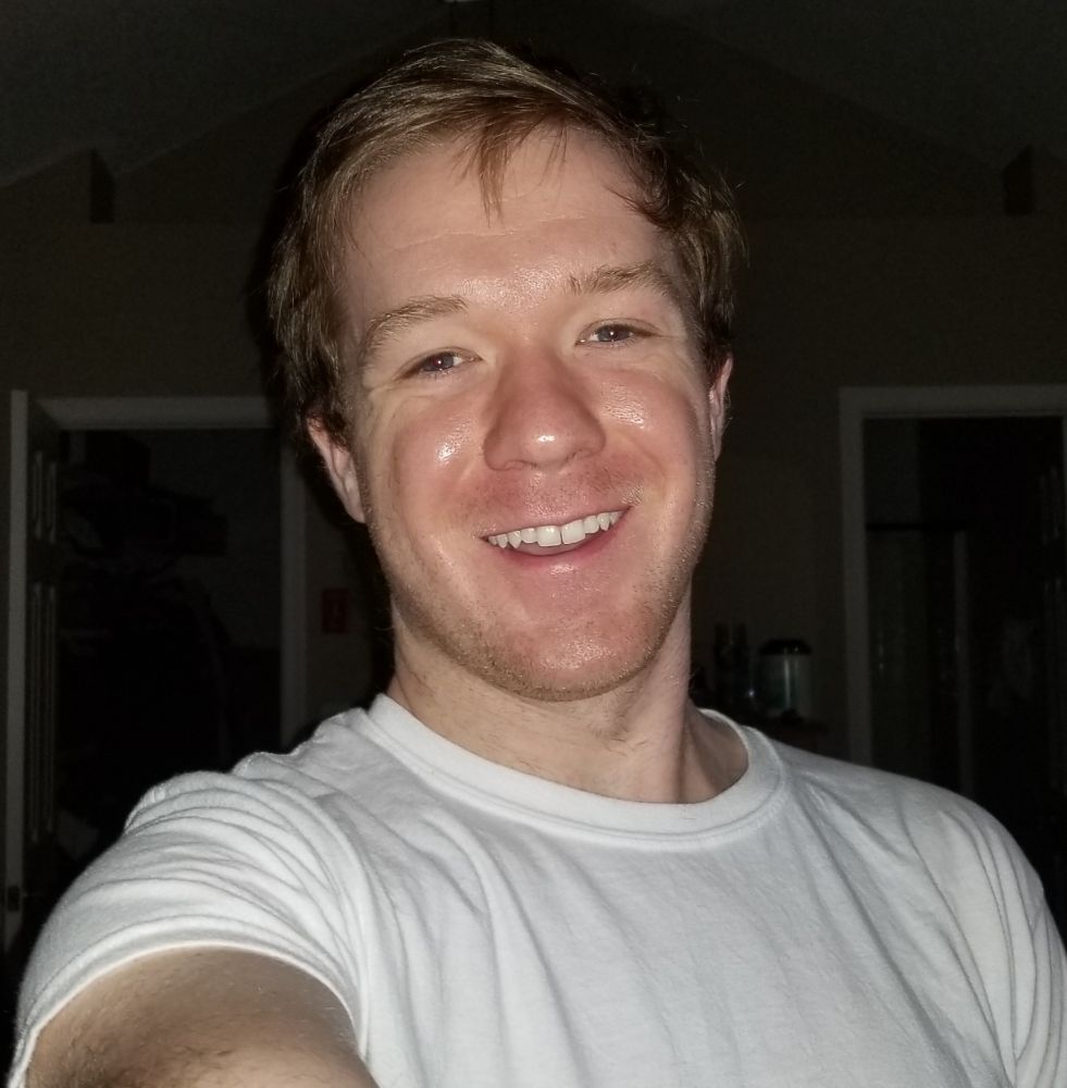 2020 selfie of a guy in his 20s with brown hair smiling and wearing a white t-shirt