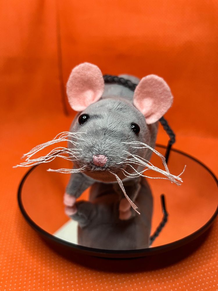 A gray rat doll standing on a mirrored platform. She has a gark gray tail, black eyes, and a pink nose.