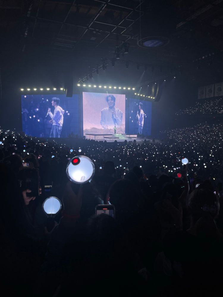 A picture of the stage while J-Hope is performing. He is smiling on one screen while standing in the middle of the platforms.