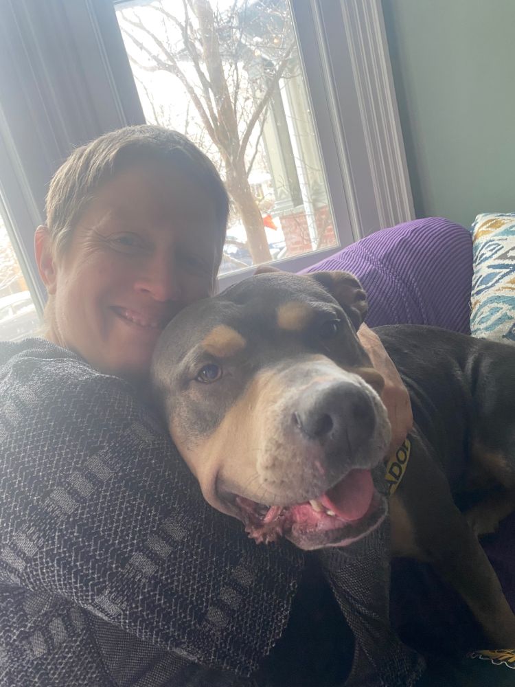 Woman cuddling a Rottweiler/pitbull mix on the couch.