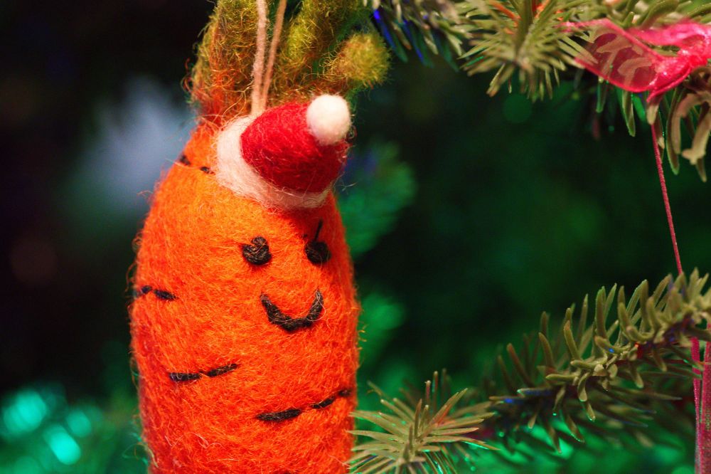 A close-up of a carrot christmas tree decoration with a small santa hat and smiley face, hanging on a christmas tree