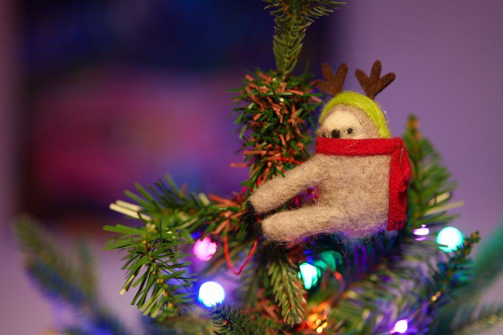 a close-up of a sloth christmas tree decoration, holding on to the tree core, with a red scarf and antlers