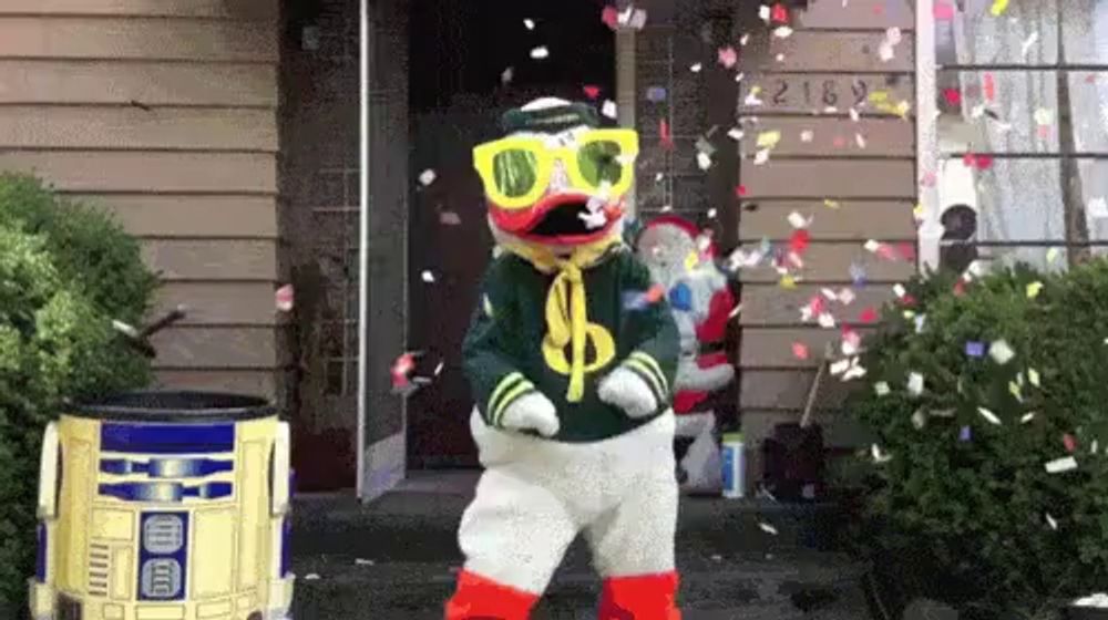 a duck mascot is dancing in front of a house while confetti is falling from the sky .